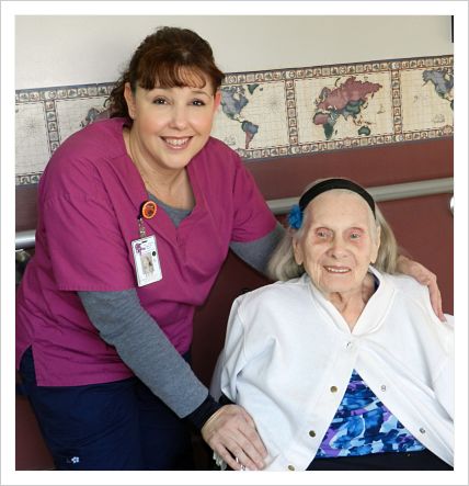 A female nurse sitting with a female elderly patient. They are both smiling.