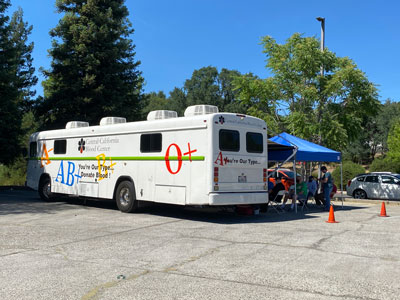 Picture of Blood Drive bus in a parking lot and a tent is set up next to it with two cones.