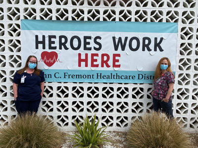 Picture of two females Nurses standing outside, wearing mask, and standing in front of a banner that says:
HEROES WORK HERE
John C. Freemont Healthcare District