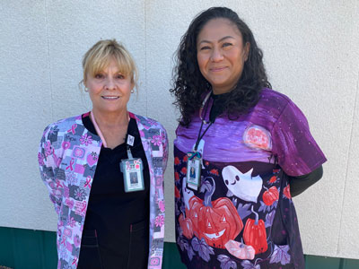 Two smiling female Nurses standing outside.