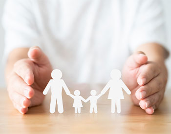 Hand protecting family on wood table. Healthcare and life insurance concept