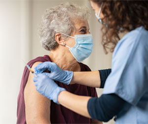 Picture of a female Nurse cleaning an elderly woman's arm before she gives her the Covid-19 Vaccine.