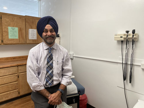 Picture of smiling Dr. Loveneet Singh sitting in a doctor's office.